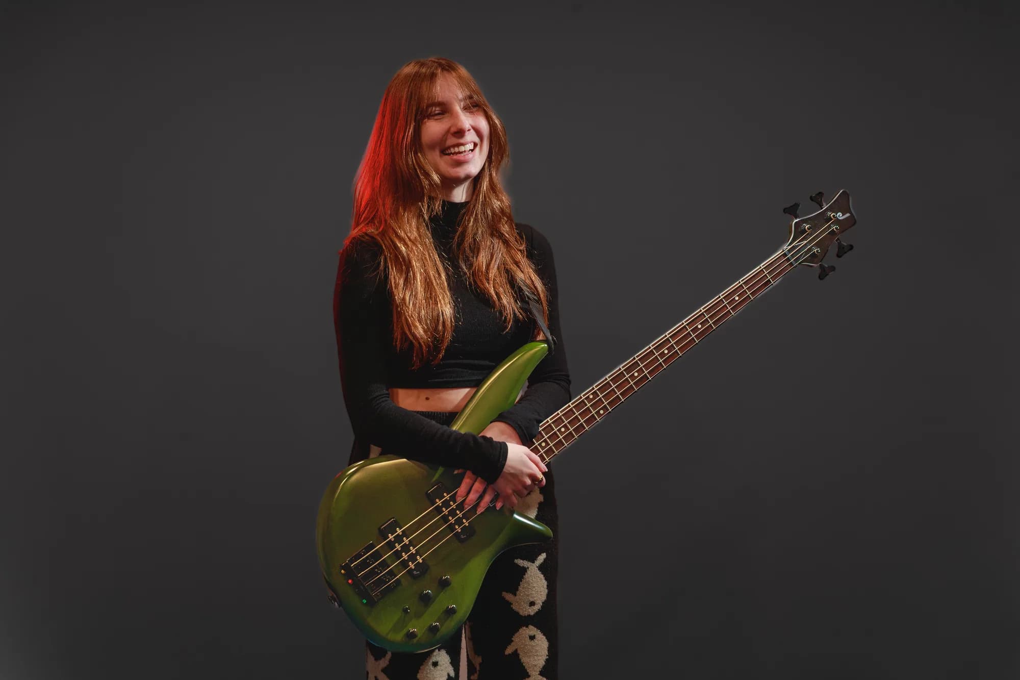 Tori Morley laughing while holding a green bass in studio.