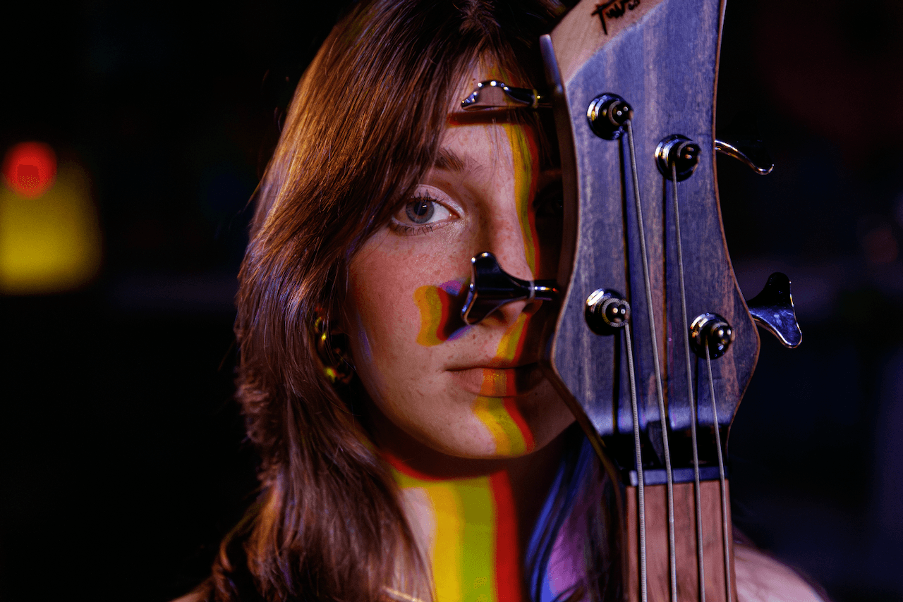Portrait of Tori Morley lit with prism color bands across her face and bass headstock.